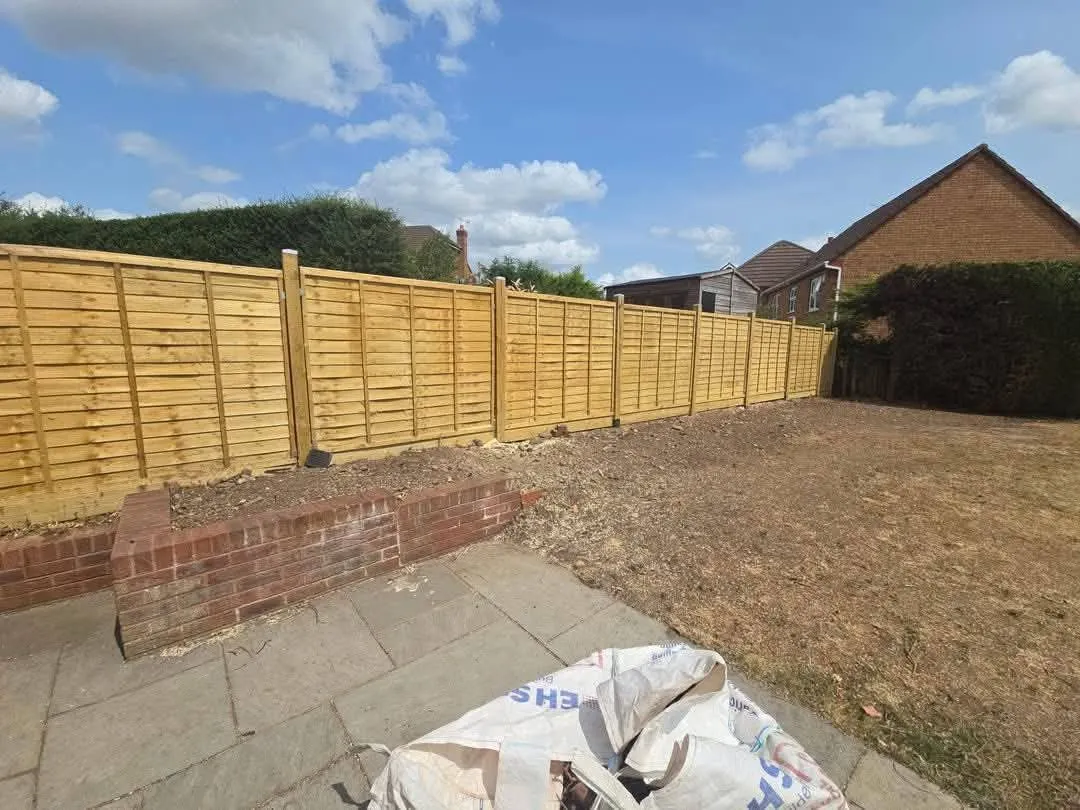 New golden timber lap-panel fence running behind the same low brick wall and stone patio